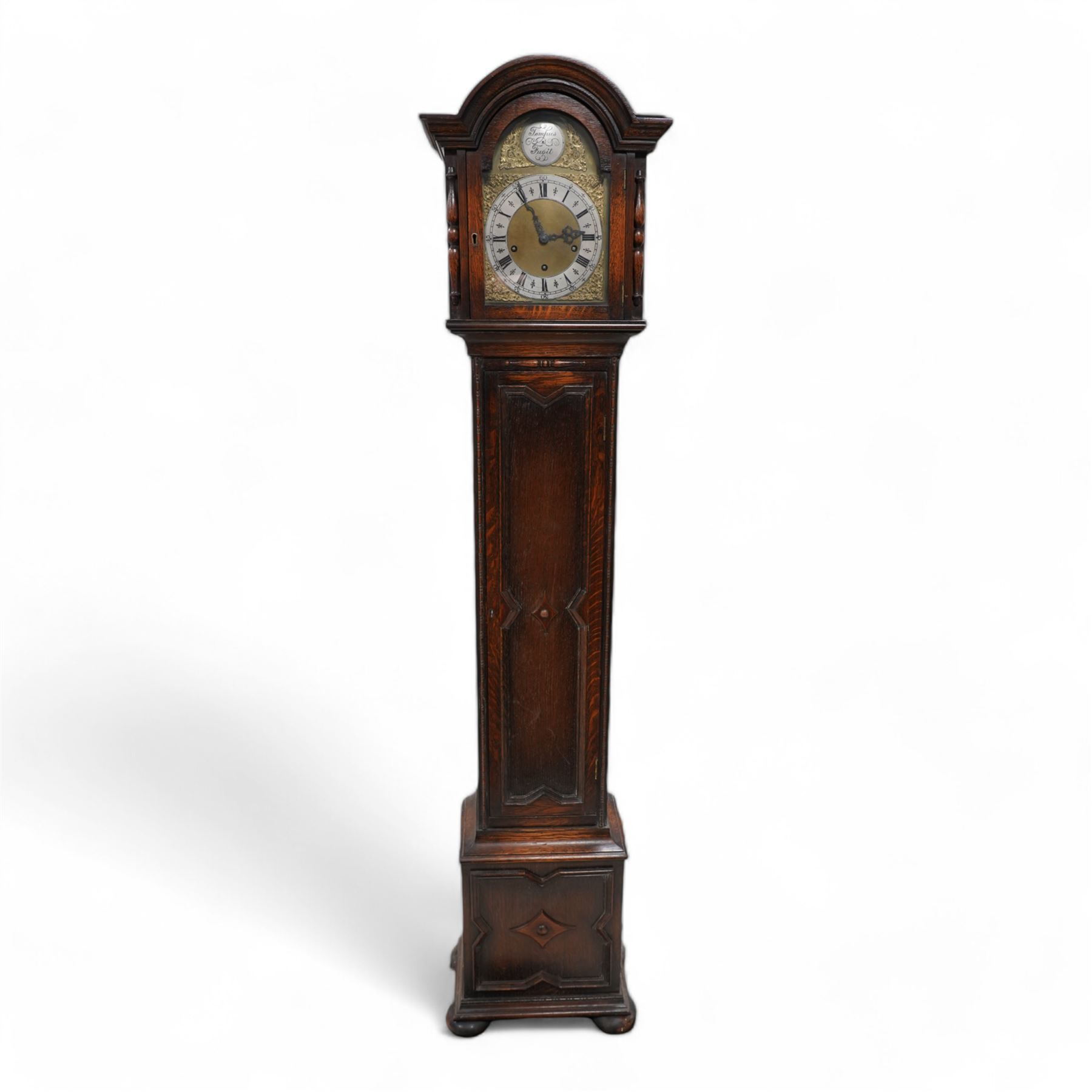 Oak cased 8-day grandmother clock c 1930 - with a broken arched pediment and break arch hood door flanked by turned pilasters, carved full length trunk door on a short plinth raised on bun feet, brass dial with cast spandrels, matted dial centre and silvered chapter with Roman numerals, three train spring driven movement chiming the quarters and hours on 8 gong rods.  With pendulum.