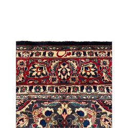 Persian Kashan indigo ground carpet, large central rosette medallion decorated with alternating palmettes, the surrounding field and spandrels with overall floral design depicting trailing branches and stylised plant motifs, crimson ground border with trailing floral pattern, enclosed within guard stripes 