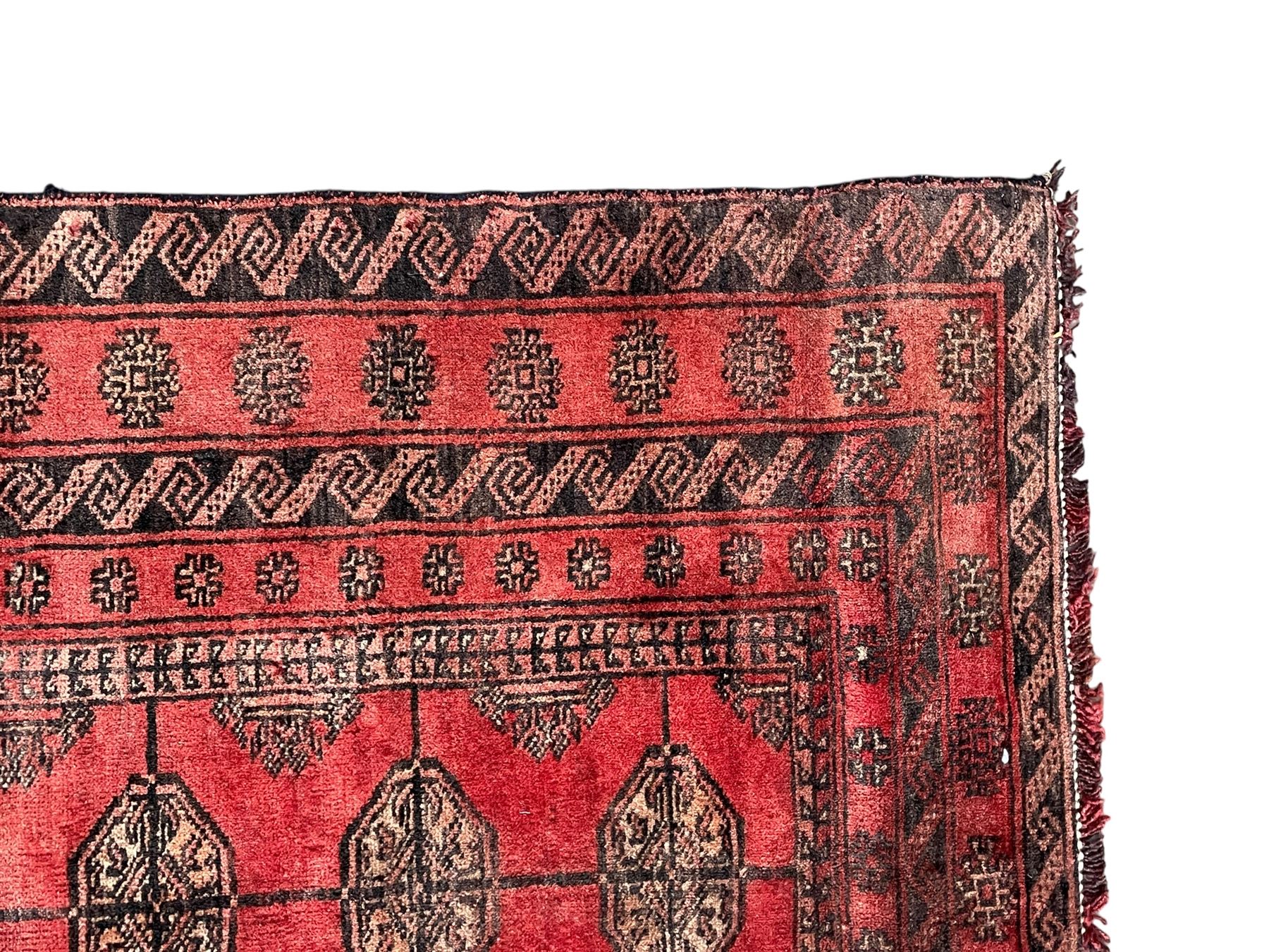 Afghan Bokhara red ground rug, the field decorated with three rows of Gul motifs, within multiple band borders decorated with trailing hook and geometric motifs 