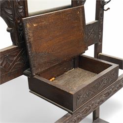 Late Victorian heavily carved oak hall stand, the scrollwork pediment with carved lion's head, bevelled mirror plate flanked by carved dragon motifs, over hinged storage compartment and umbrella stands with drip trays, on turned front supports