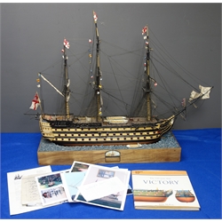  Wooden solid hull scale model of HMS Victory, furl rigged flying signal flags, with lifeboat on stand with ocean textured top, built c1990, with photos of build, plans and 1vol 'Anatomy of The 110 Gun Ship Victory' by John McKay, L104cm, H77cm  