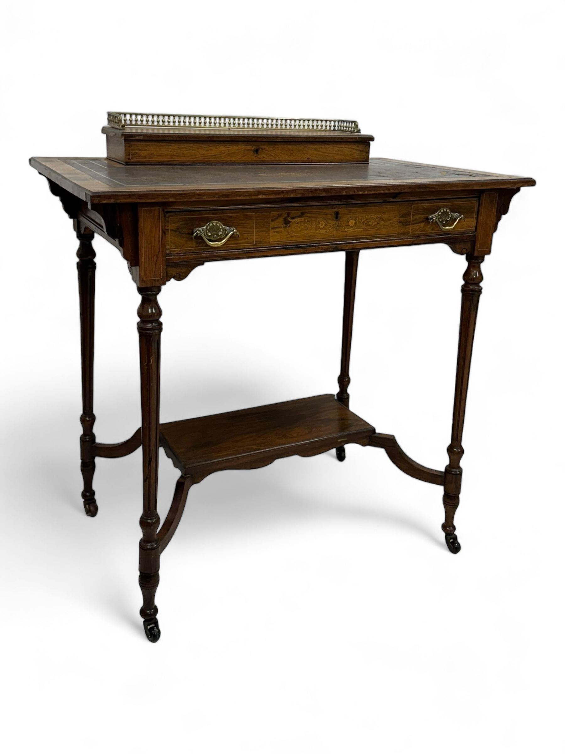 Late Victorian walnut writing table, rectangular leather-inset top surmounted by a brass gallery, fitted with a single frieze drawer, raised on turned tapering supports with lower undertier and ceramic castors