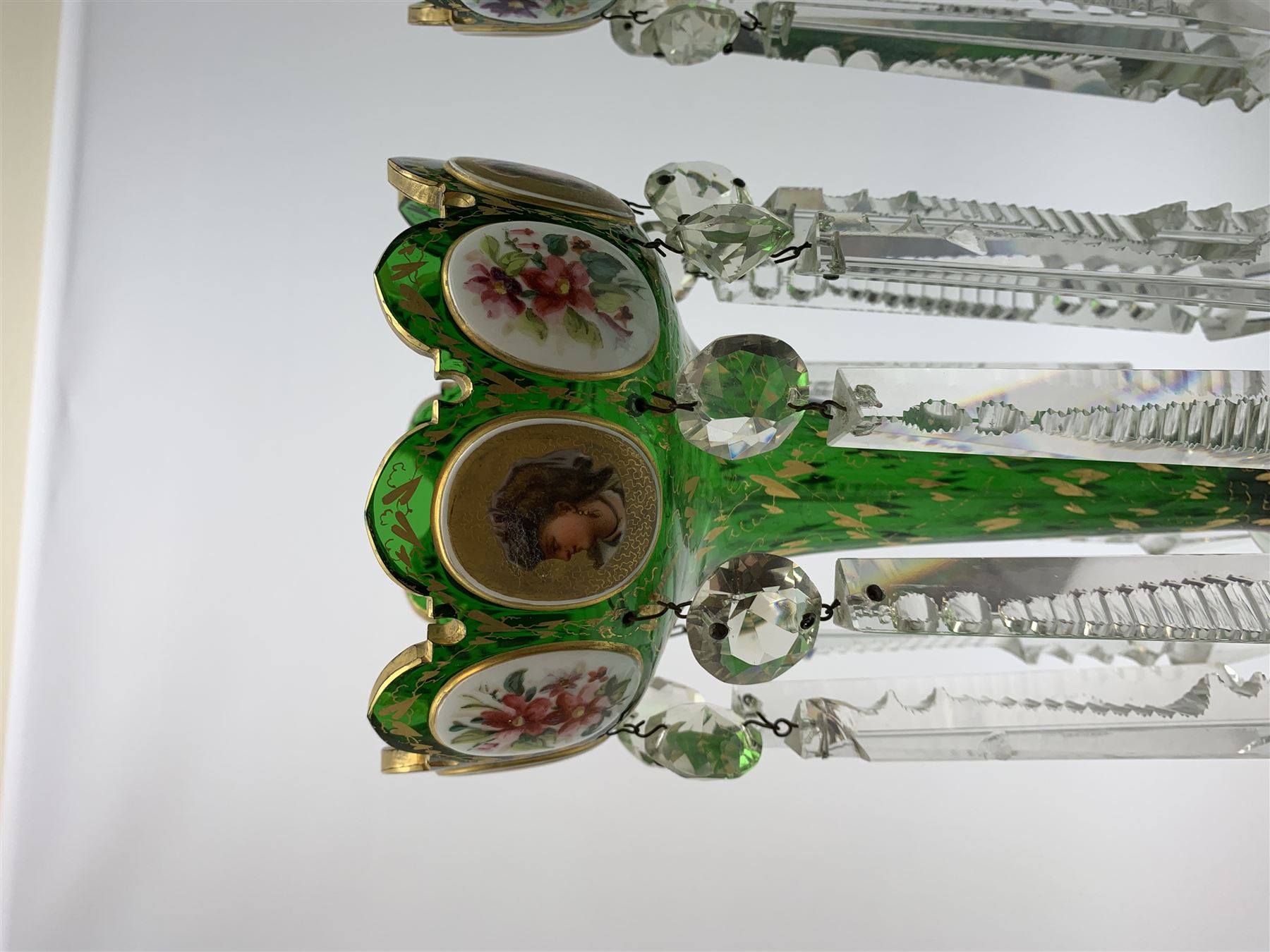 Pair of 19th century Bohemian green glass lustres, the castellated bowls decorated with overlaid panels of flowers and female portraits, upon tapering stems and overlaid spreading feet, heightened throughout with gilt, each supporting ten prismatic drops, H35cm
