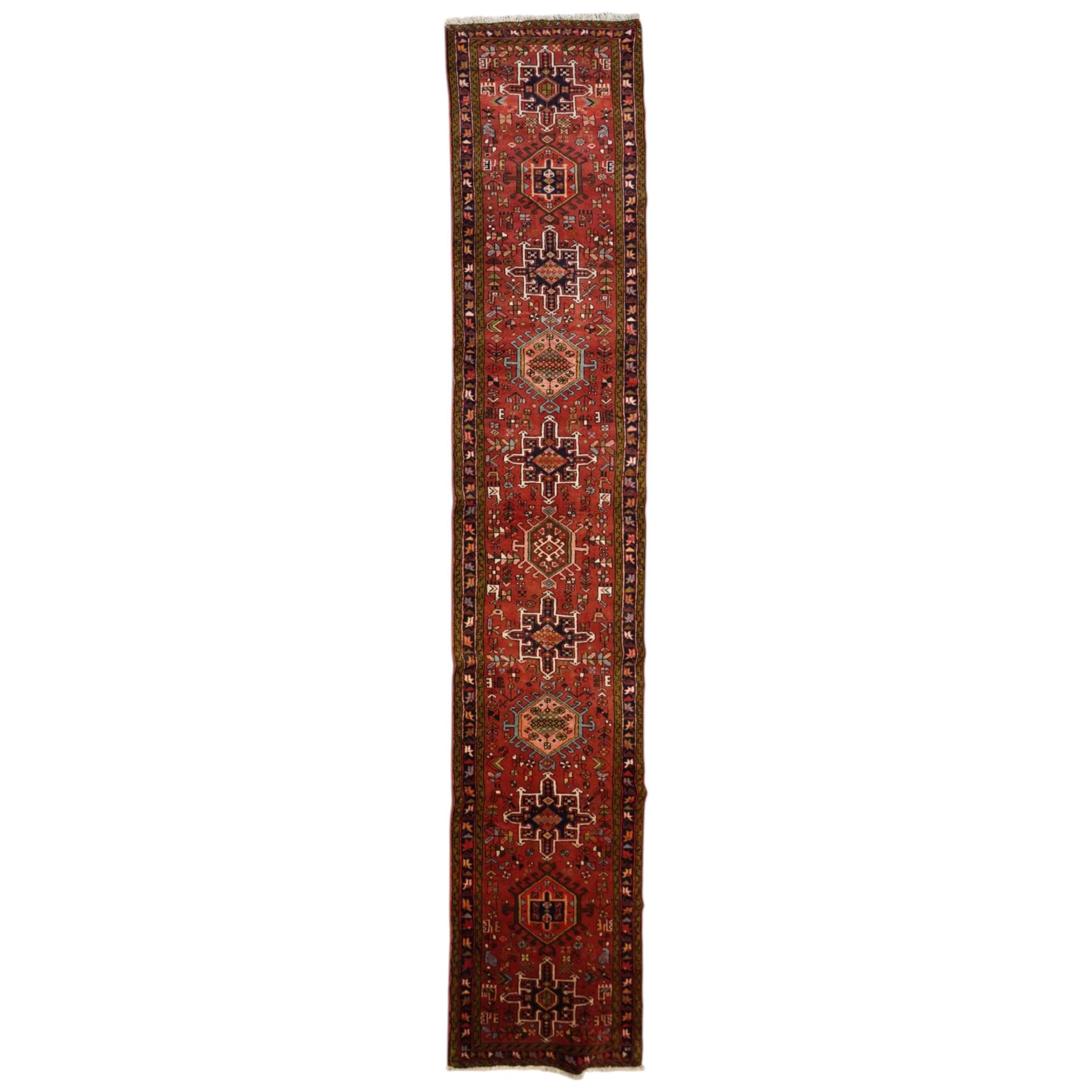 North West Persian Karajeh hand-knotted runner, madder red field with a series of shaped hexagonal medallions and cruciform motifs each enclosing geometric rosette devices linked by angular vine elements, field populated with stylized tribal ornaments, within narrow multiple borders decorated with repeating angular motifs framed by guard stripes of geometric devices, with cotton fringe ends  