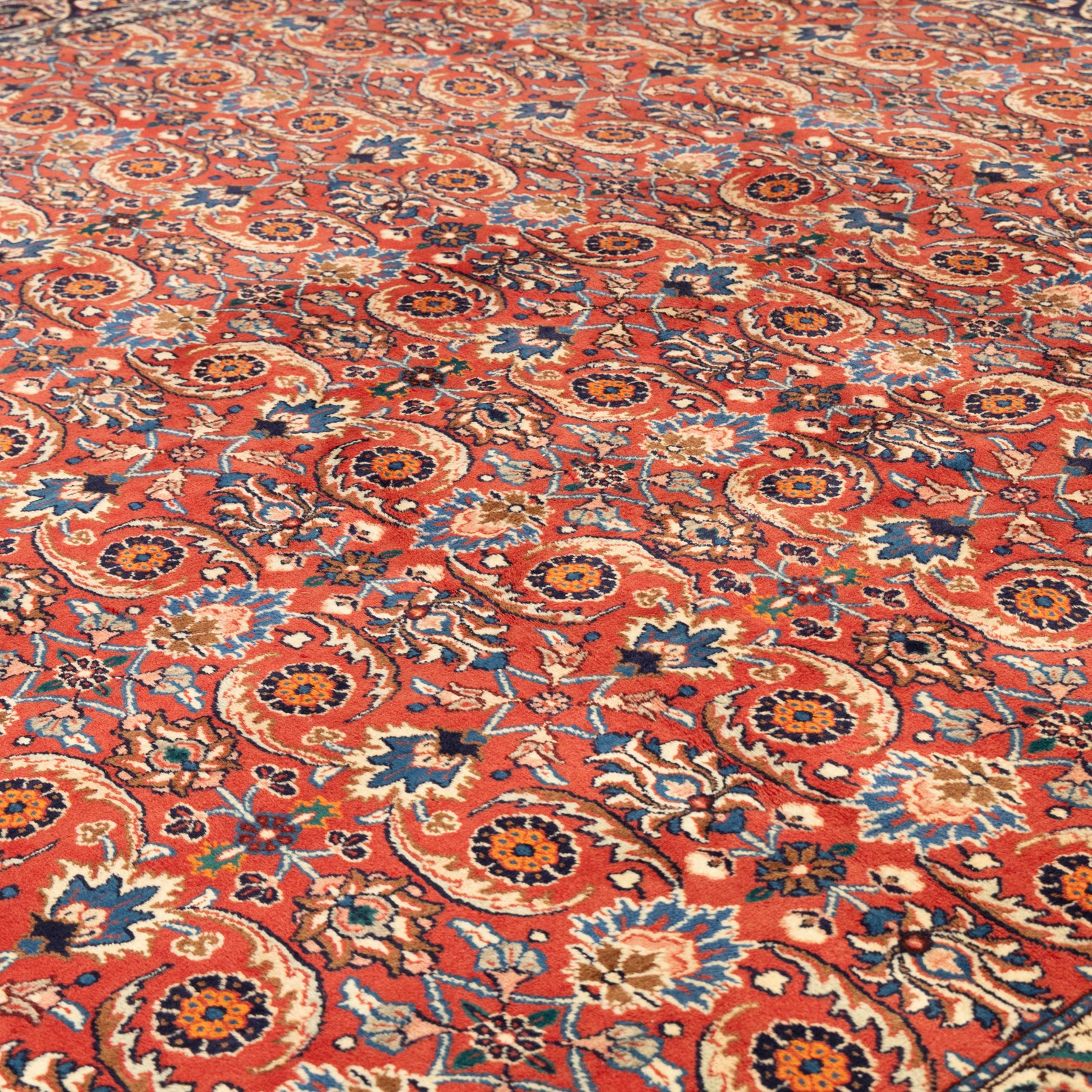 North West Persian carpet, the red field decorated with an all over repeating design of palmettes, rosettes and curling serrated leaves in indigo, ivory and ochre tones, enclosed by an indigo scrolling floral border and ivory flowerhead guard bands