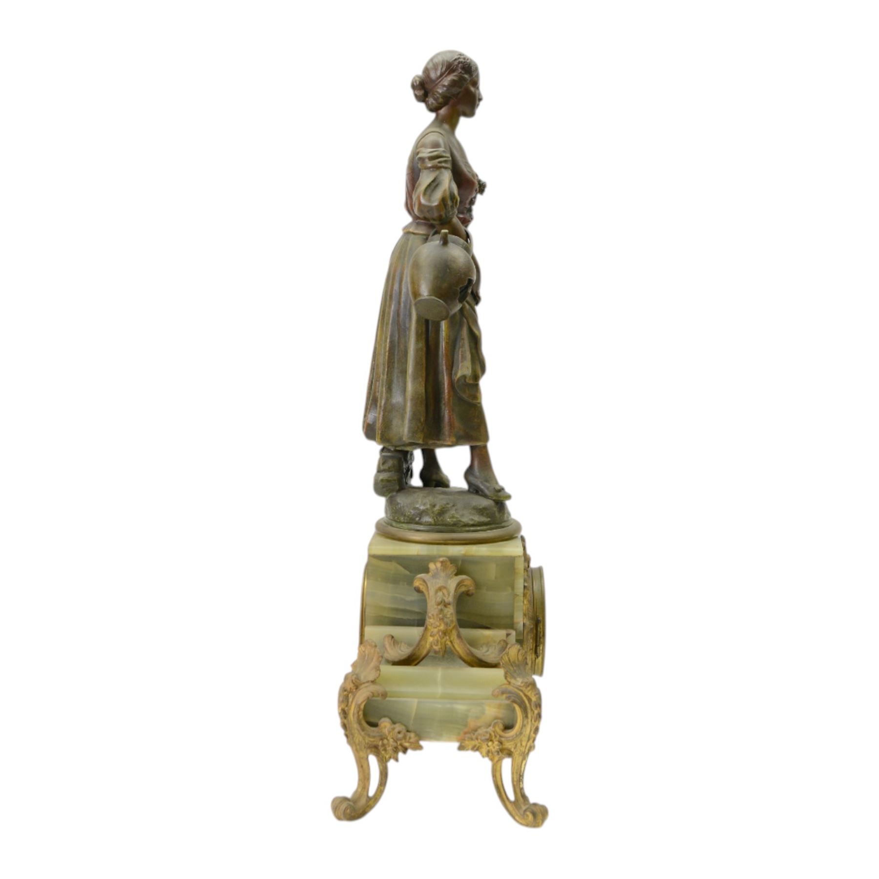French-Edwardian green onyx clock garniture with a shaped case surmounted by a cast patinated figure of  a maiden in 18th century dress, with gilded scroll feet and conforming mounts, porcelain dial with Arabic numerals and floral decoration, twin train rack striking movement sounding the hours and half-hours on a bell, with a matching pair of five light candelabra. With pendulum.    