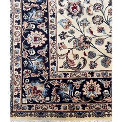 North East Persian Meshed hand-knotted rug, ivory field with scrolling vines, palmettes, and rosettes in shades of blue and brown, within a dark blue border of palmettes and flowerheads between multiple guard stripes, with cotton fringe ends  
