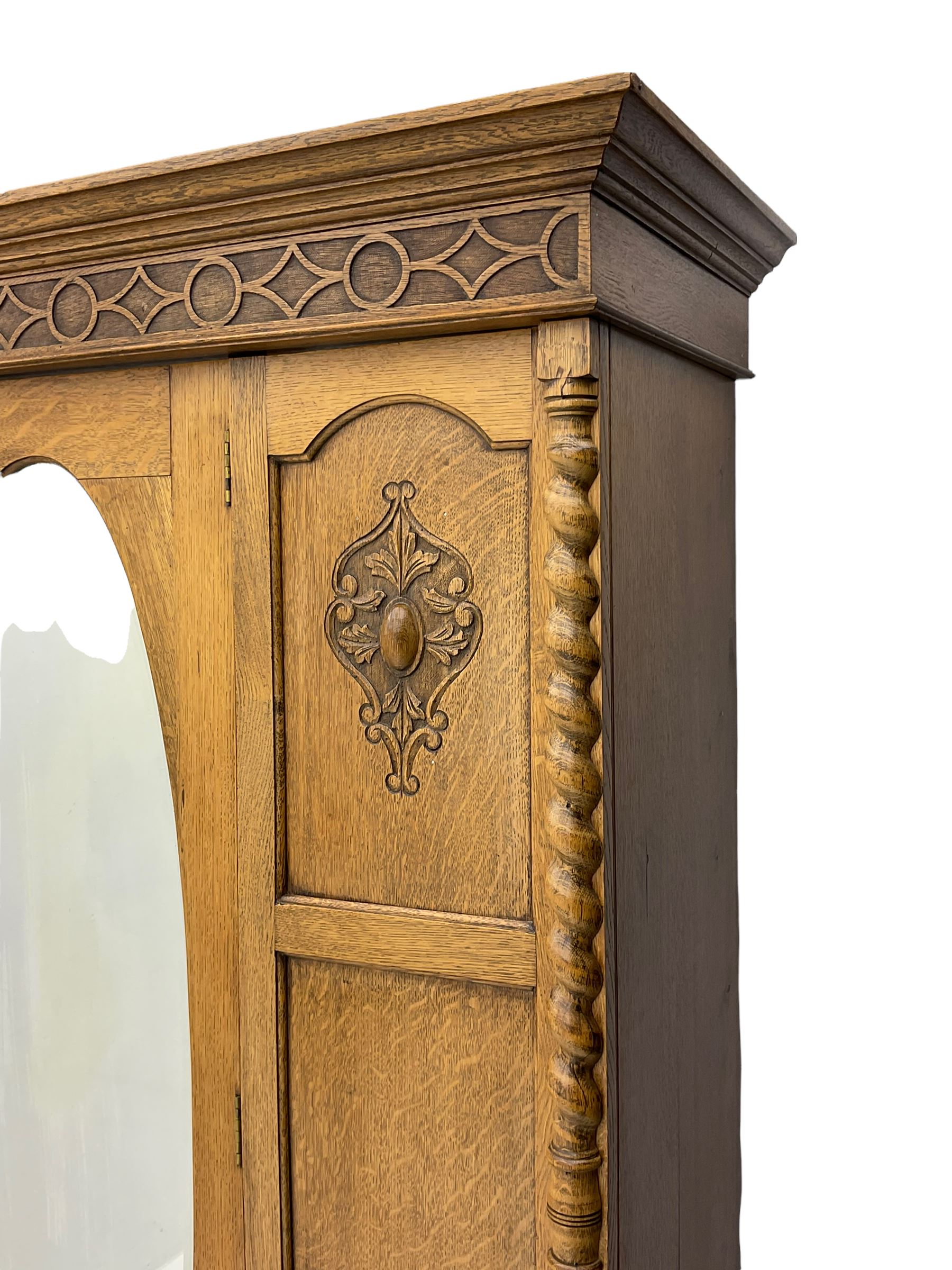Early 20th century oak wardrobe, projecting cornice of blind fret-work frieze, oval bevel edge mirror door, half spiral turned pilasters, drawer to base with mouldings, on turned bun feet