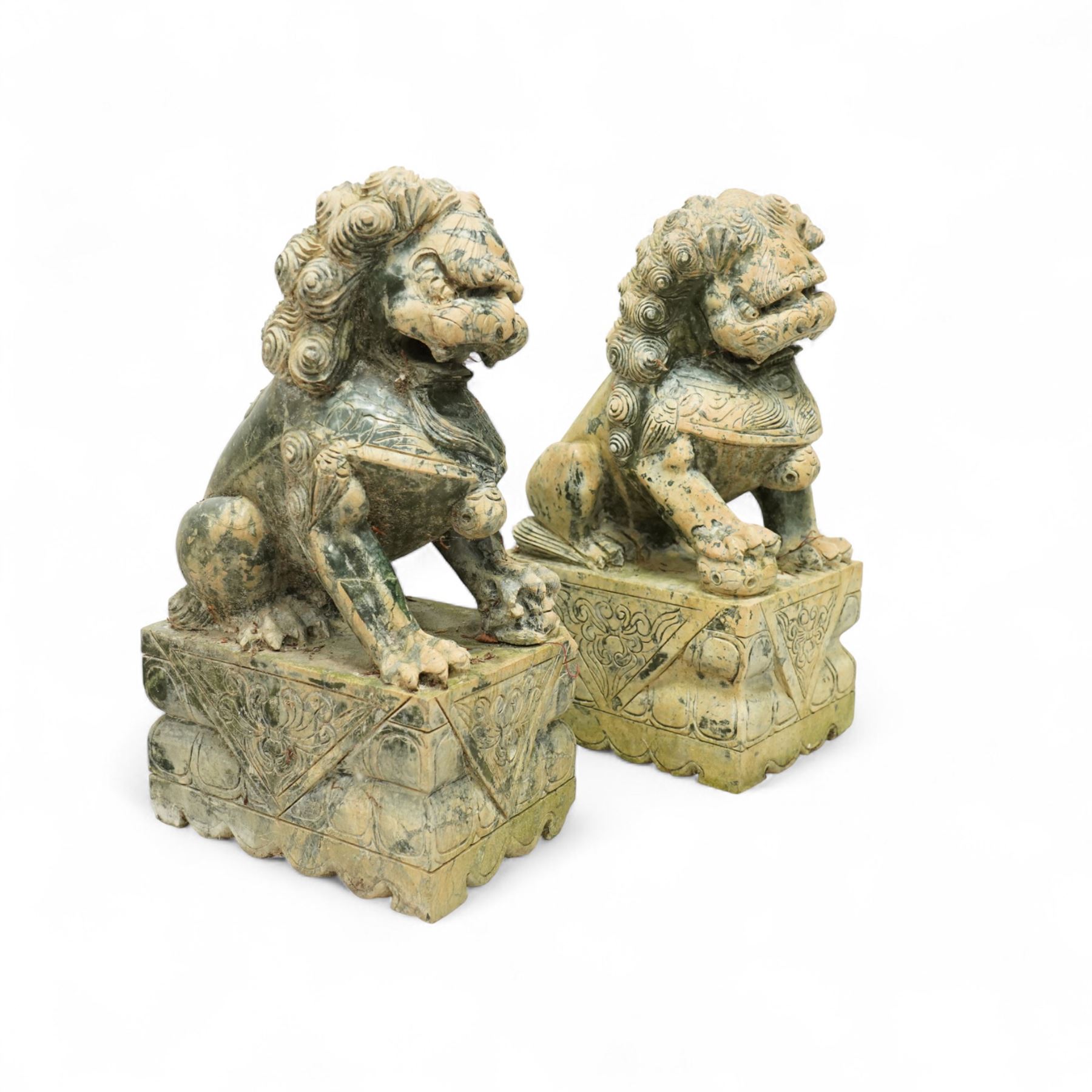 Pair of Chinese hardstone carved Foo dogs, each finely carved seated on rectangular plinth bases with detailed manes, collars and bells, the male with paw resting on a ball, the female with cub, in mottled green stone resembling jade