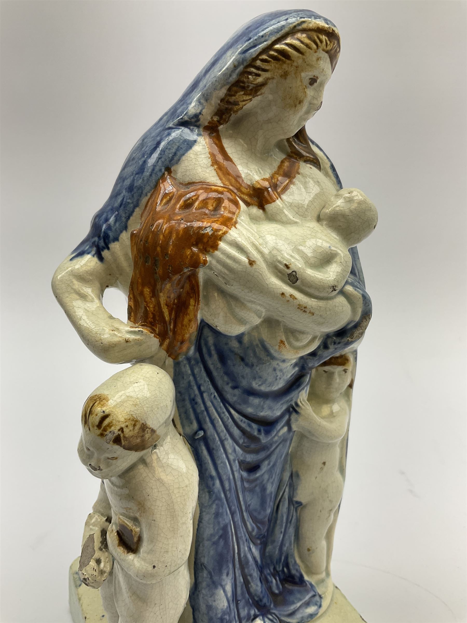 Late 18th century Prattware figure representing Charity, modelled as a mother with baby in her arms and two small children clutching at her robes, upon a square base, overall H21cm.