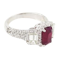 18ct white gold ruby and diamond trilogy ring, single emerald cut ruby of approx 1.85 carat, with a single emerald cut diamond set either side, all surrounded by round brilliant cut diamonds, the shoulders set with three rows of round brilliant cut diamonds, principal two emerald cut diamonds approx 1.10 carat