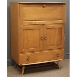  Mid 20th century Ercol elm and beech serving cabinet, fall front enclosing shelf compartments, two door cupboard with an adjustable shelf, above a long drawer, turned handles, four turned tapering supports with stretchers, W83cm, H114cm, D51cm    