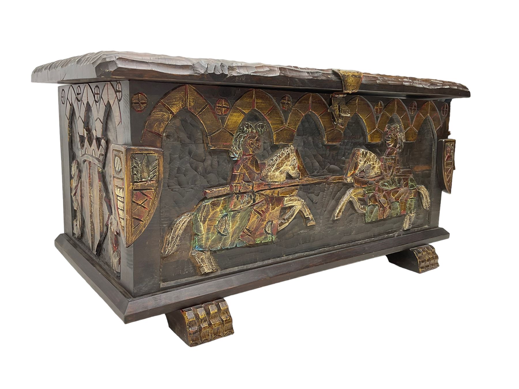 Carved wooden blanket chest, the tooled hinged lid with shaped metal strap hinges and catch, the front carved with arcade over two medieval jousters, on carved sledge feet
