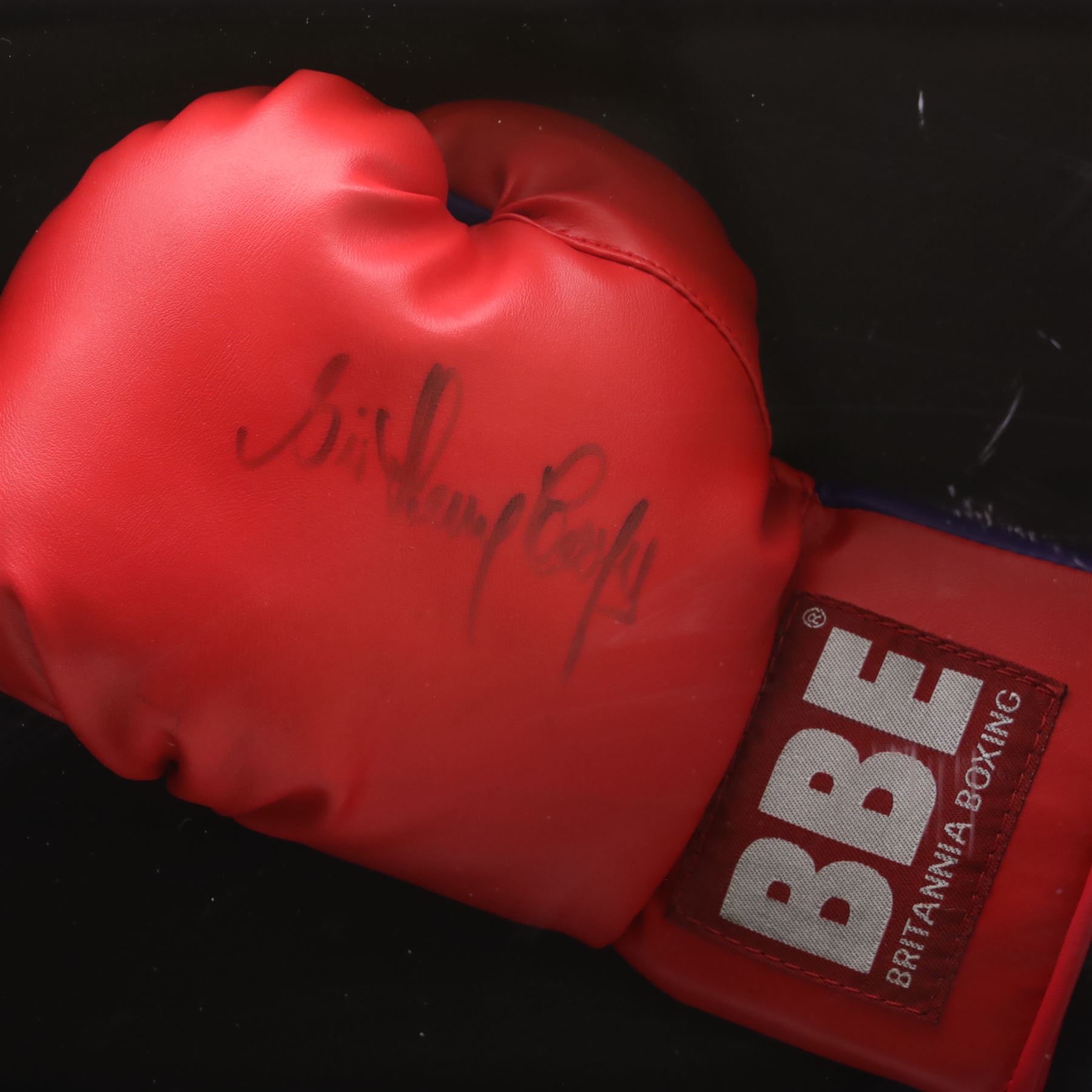 Framed display contained a single BBE Britannia boxing glove, signed by Sir Henry Cooper, displayed with a black and white print of Cooper with Ali on the ropes, with certificate of authenticity by Superstars For You, frame H59cm