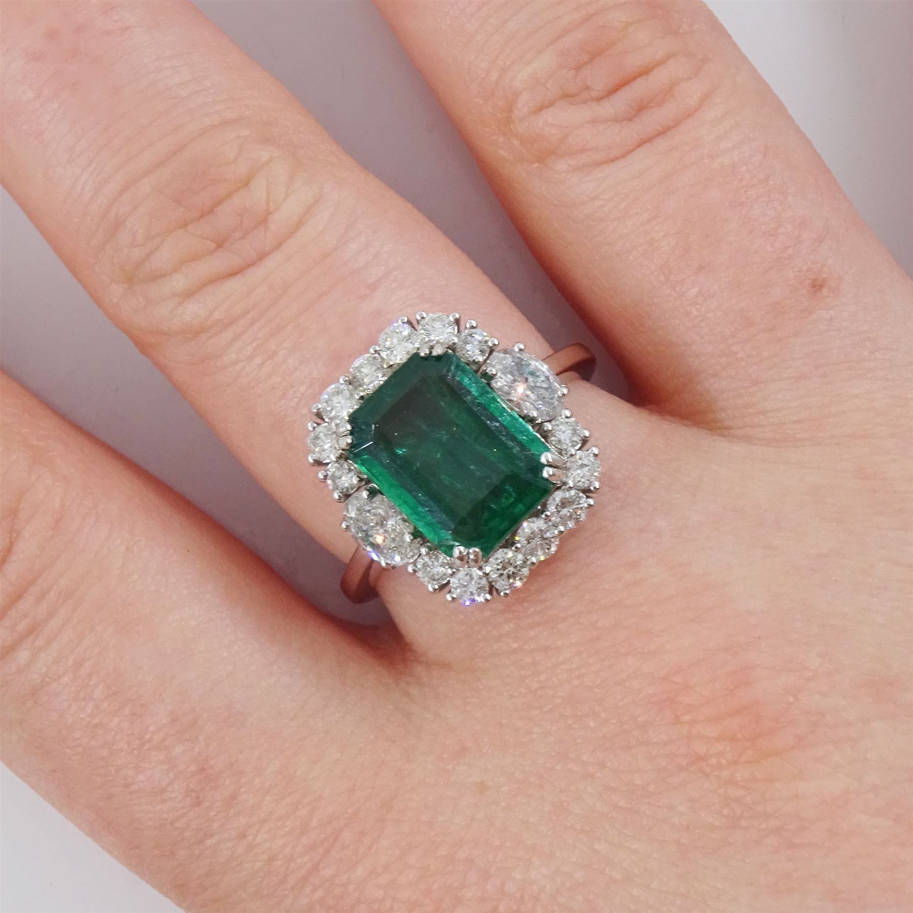 18ct white gold emerald and diamond cluster ring, the octagonal cut emerald of approx 2.85 carat, with an oval cut diamond set either side and round brilliant cut diamond surround, stamped, total diamond weight approx 1.05 carat