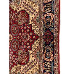 Persian red ground carpet, shaped medallion decorated with central latticework of flower heads, the field decorated in segments of trailing flower head bands, tree and lotus flowers, overall floral design spandrels, the border decorated with further floral motifs in wreaths interspaced with scrolled motifs, within guard bands