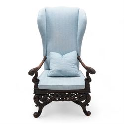 Carolean design walnut and oak wingback open armchair, the high wingback upholstered in light blue herringbone fabric, acanthus leaf carved arms with scrolled terminals and on scrolled supports, cane work seat with squab cushion and scatter cushion, the lower rail carved and pierced with putti holding crown surrounded by curled acanthus leaves, leaf carved S-scroll supports united by Scrolled X-framed stretchers 