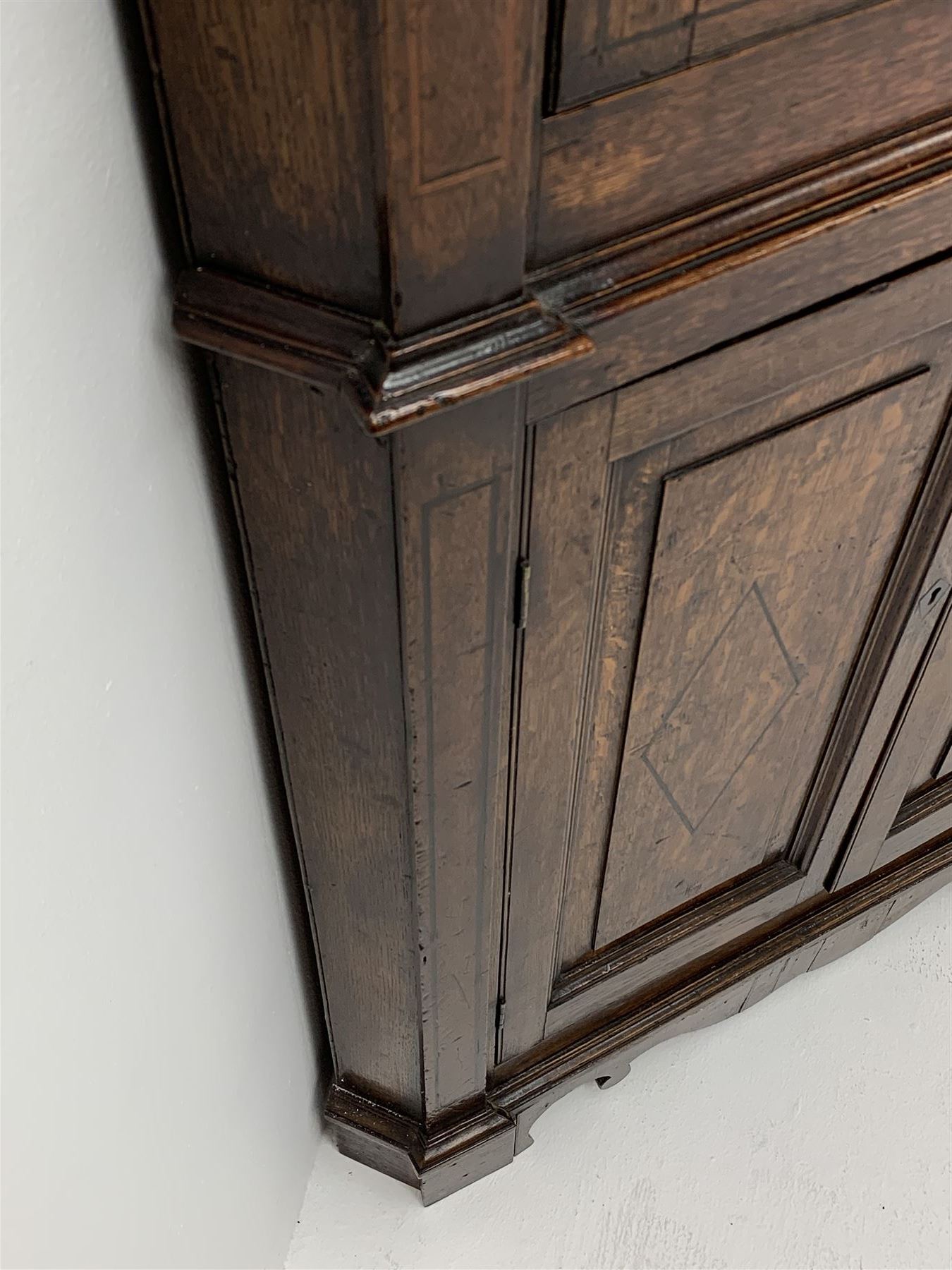 George III oak floor standing corner cabinet, scrolled swan neck pediment with central finial over astragal glazed door, painted interior fitted with three shaped shelves, the lower section fitted with single shaped shelf enclosed by two fielded panel doors inlaid lozenges, on bracket feet, H195cm, W77cm