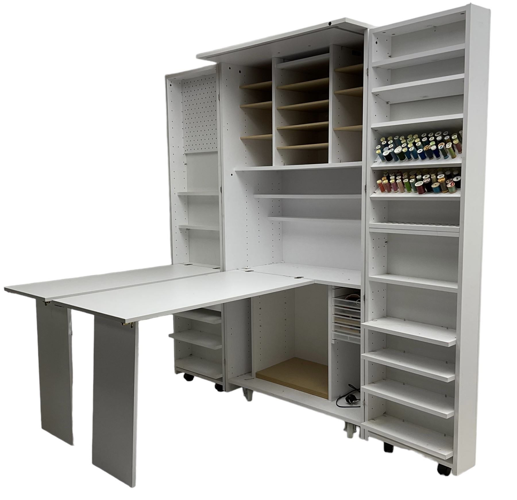 Large white finish sewing cabinet, enclosed by two doors fitted with thread holders and shelves, the interior fitted with shelves and sliding trays, with fold down work surfaces 