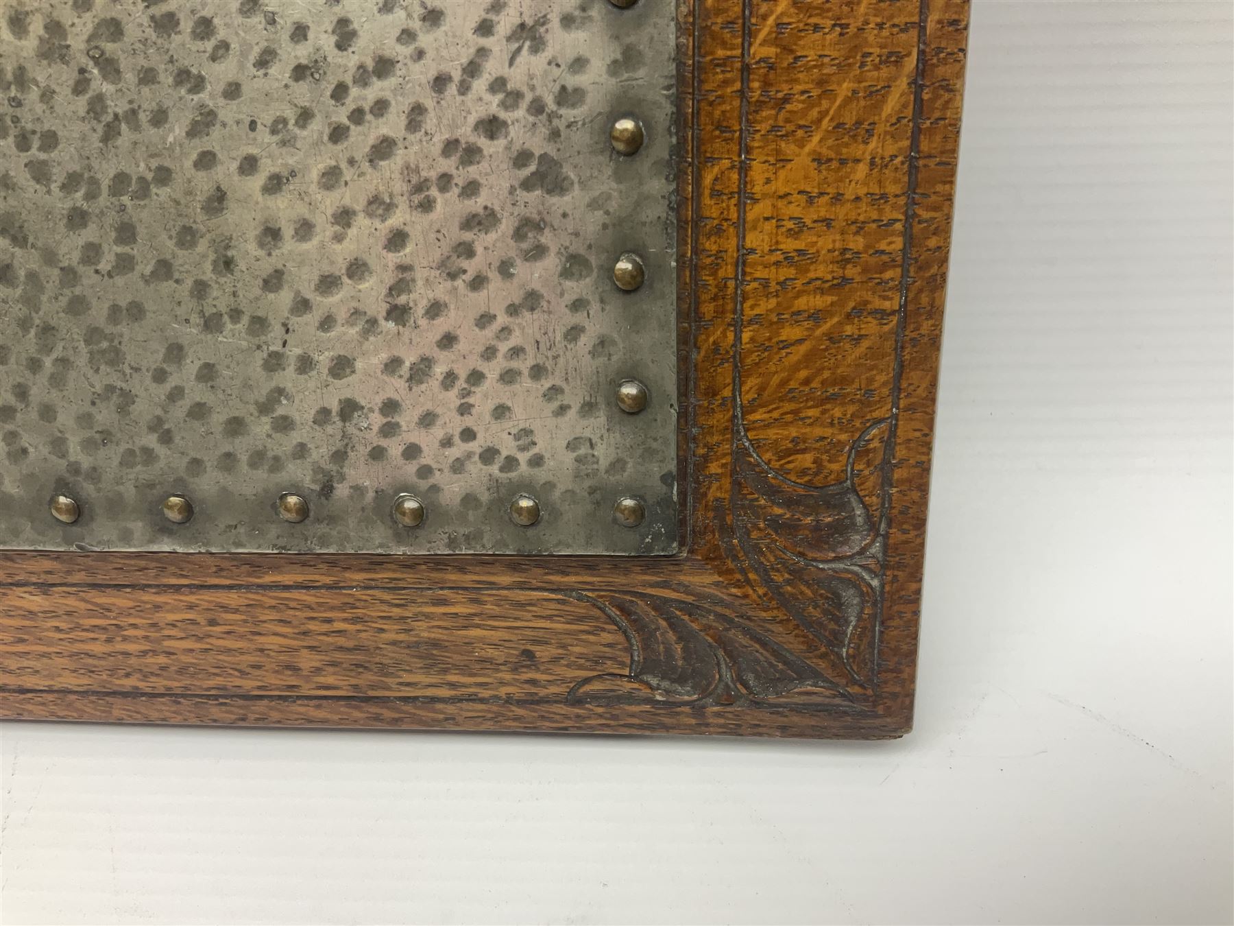 Arts and Crafts oak stand by Arthur Simpson of Kendal, of rectangular form with central hammered pewter panel, surrounded by a border with carved foliate corners, upon two bar supports, bearing label detailed 