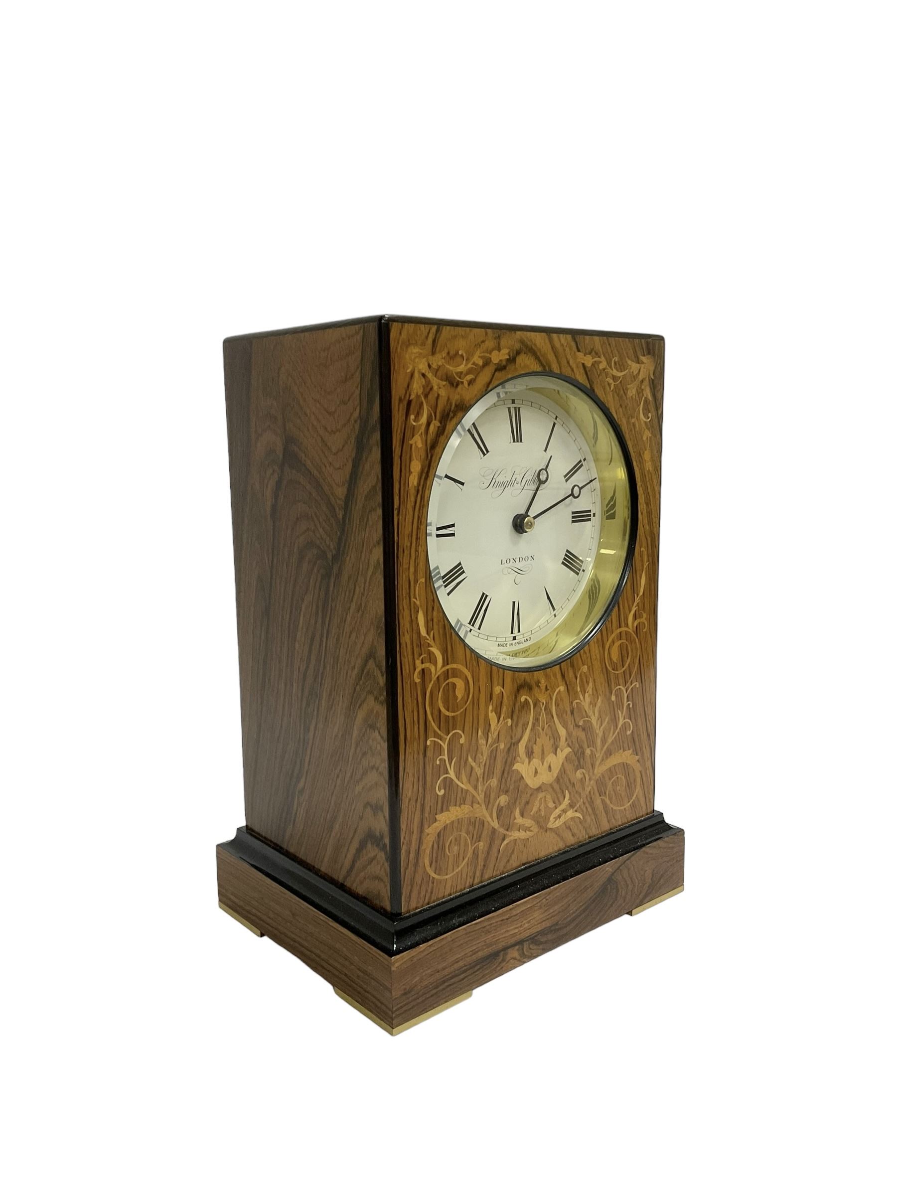 Knight & Gibbins London - 20th century 8-day marquetry inlaid mantle clock in rectangular case on a short plinth, glazed circular dial with Roman numerals and steel moon hands, two train striking movement with a floating balance escapement striking the hours and half hours on a bell, rear set and wound. With key.   