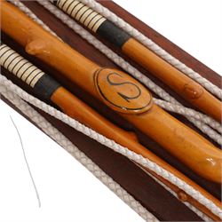 A Woodcock Hill - 20th century travelling coaching whip, the two part yew wood twisted shaft, with leather grip and brass collar and butt cap, with makers mark below the leather handle 'A Woodcock Hill Whip Maker G.I Clothier', together with an additional thong end, mounted upon a wall mounted holder, whip 142cm 
