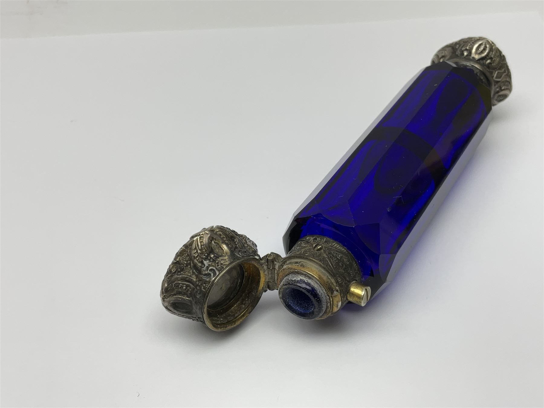 Late Victorian silver mounted ruby glass cylindrical scent bottle, with interior glass stopper, Birmingham 1900, makers mark worn, H8cm, together with a Victorian double ended cut blue glass perfume bottle mounted with white metal screw and flip caps decorated with foliate repousse detailing, H13.5cm
