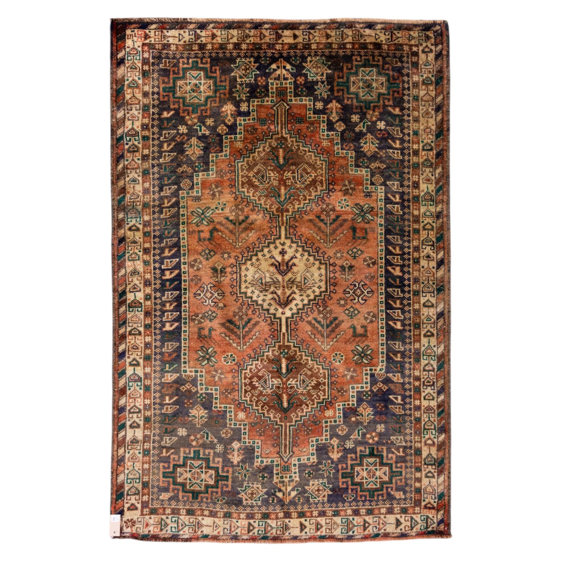South West Persian Qashqai hand-knotted rug, salmon pink field with central stepped geometric medallion with issuing stylized tree and floral motifs, surrounded by angular devices, with indigo spandrels and multiple geometric borders, fringe ends 
