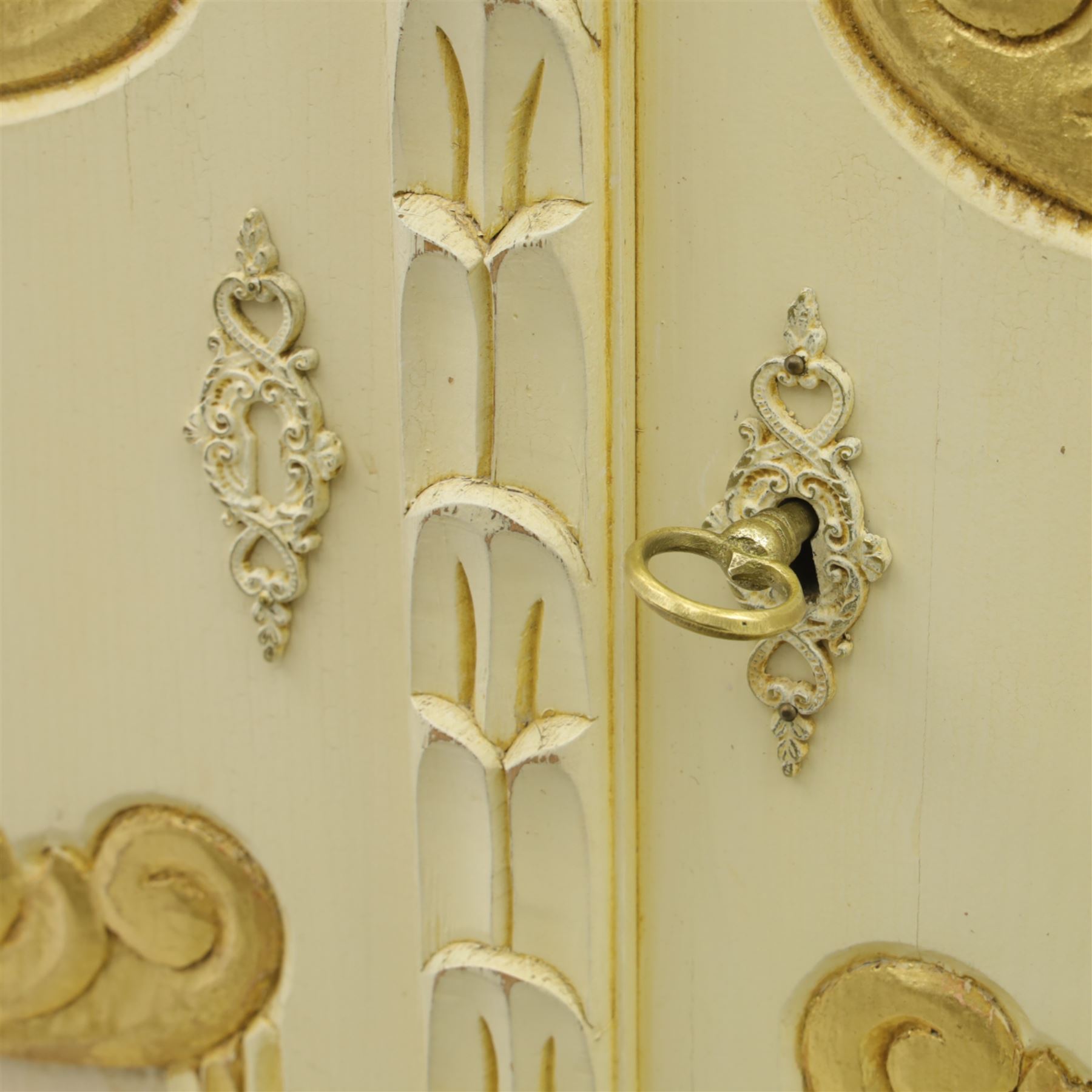 20th century French white and parcel gilt painted armoire, the shaped and scroll moulded cornice centred with a stylised foliate, the double doors with raised panel reserves applied with gilt foliate scrollwork, flanked by fluted pilasters with floral capitals, opening to a fitted interior with shelving and hanging space, raised on a moulded plinth on squat bun feet