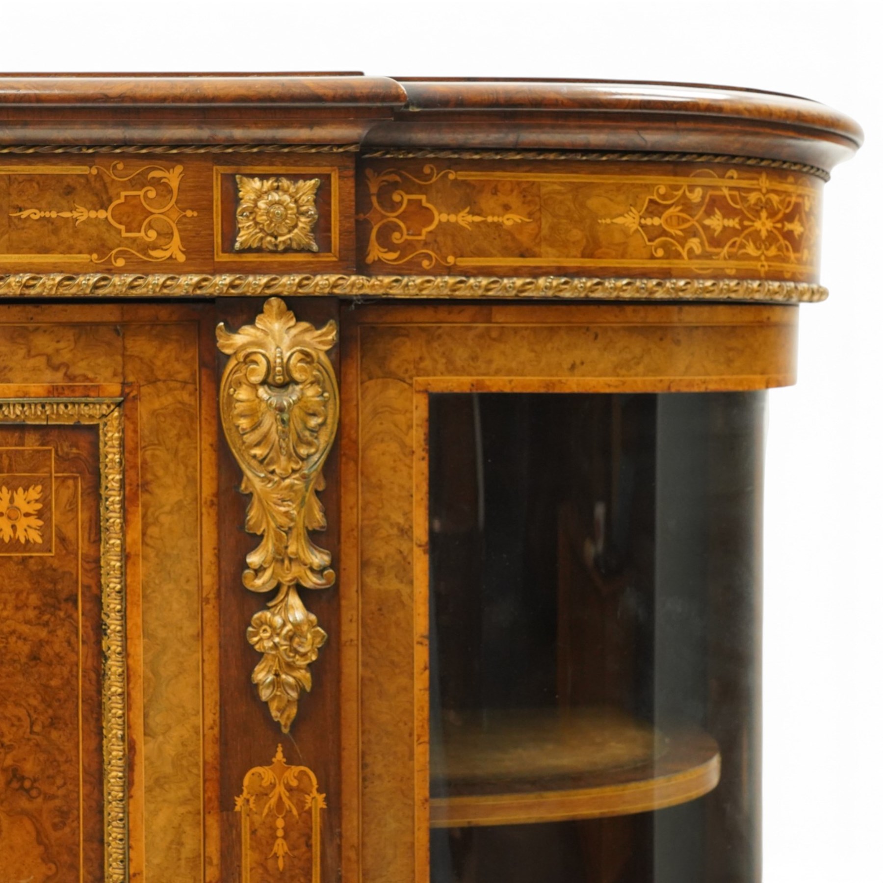 Large fine Victorian figured and burr walnut credenza, the breakfront D-shaped top with moulded edge, over an ornate frieze with inlaid Aesthetic Movement scrolling and geometric ornament, applied with gilt-metal ribbon-twist moulding and mounts, the central panelled doors profusely inlaid with scrolling foliate motifs and stringing, flanked by gilt-metal cartouche and scrolling acanthus corbel mounts, with flanking glazed bow-front side doors, on skirted base with further gilt metal foliate mounts