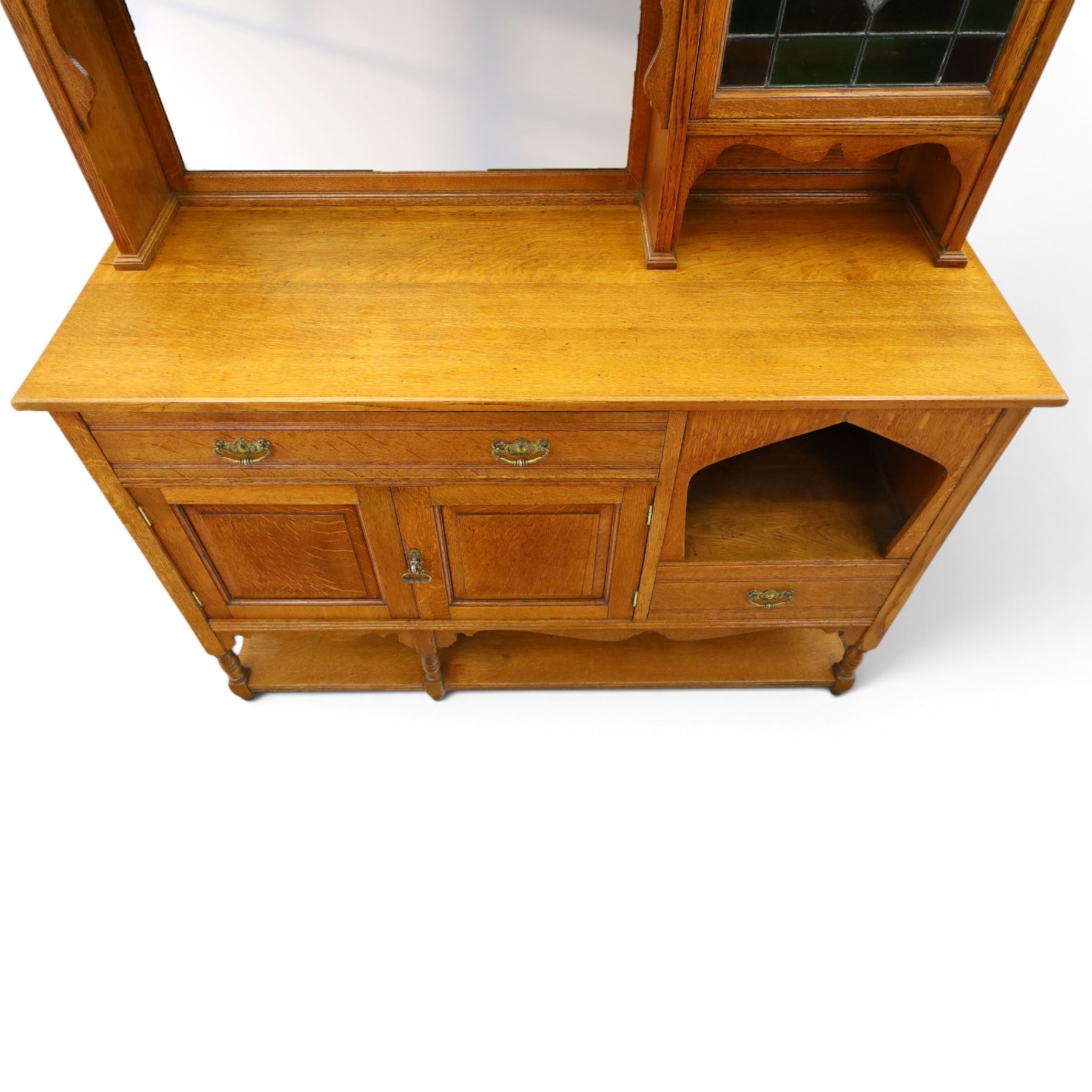 Maple & Co. - Arts & Crafts oak dresser with stained glass cupboard, raised section with pierced pediment above a mirrored back, with a stained glass fronted cupboard with fixed shelf, single long drawer, above a pair of fielded panels, with open recess above a short drawer, raised above a full length undertier with turned supports