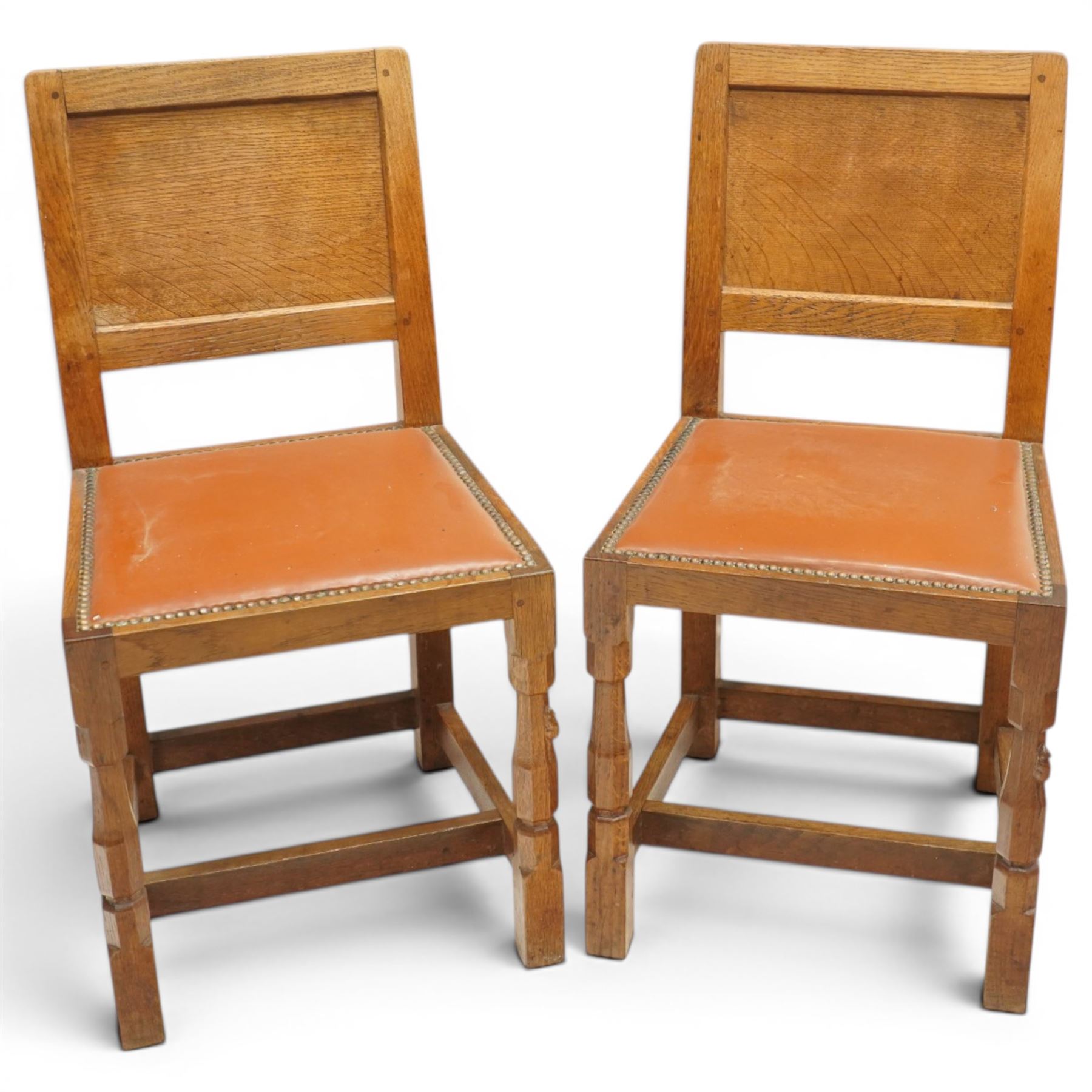 Mouseman - pair of 1940's adzed and panelled oak chairs, the rectangular adzed back-panel over seats upholstered in orange-tan leather with studwork, raised on turned octagonal supports united by box stretcher, with carved mouse signature, by the workshop of Robert Thompson of Kilburn
Provenance: purchased directly from the Kilburn workshop in the late 1940s