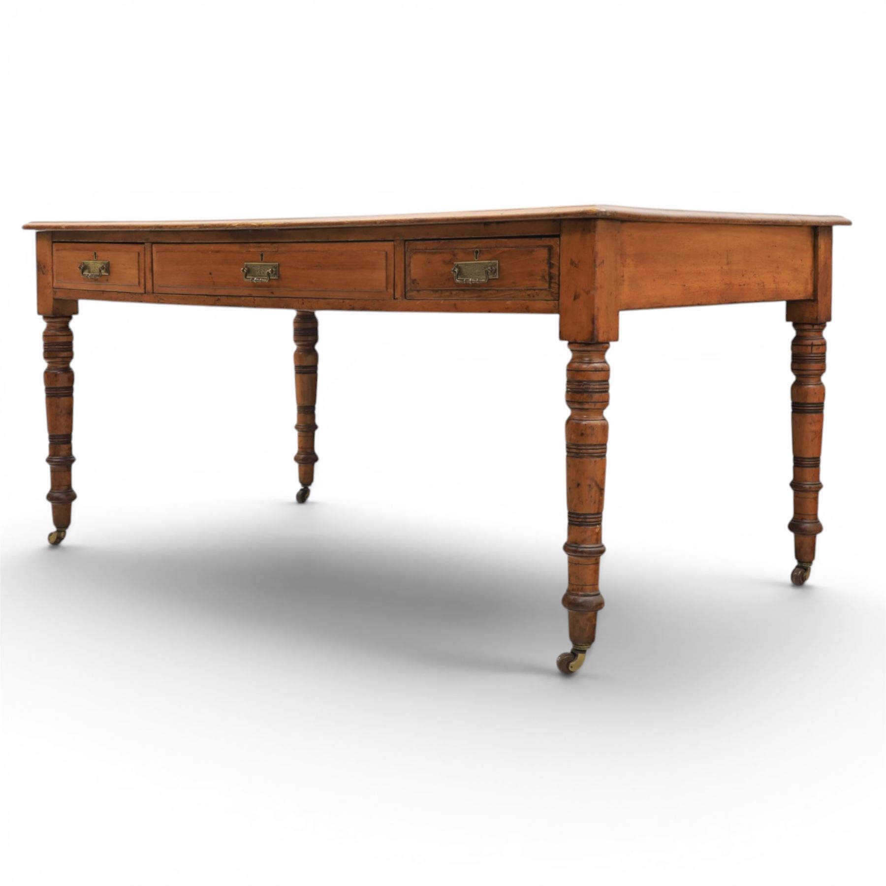 Victorian pitch pine writing table with leather inset top, rectangular top with three frieze drawers, pierced brass handles, raised on turned and fluted supports terminating in castors