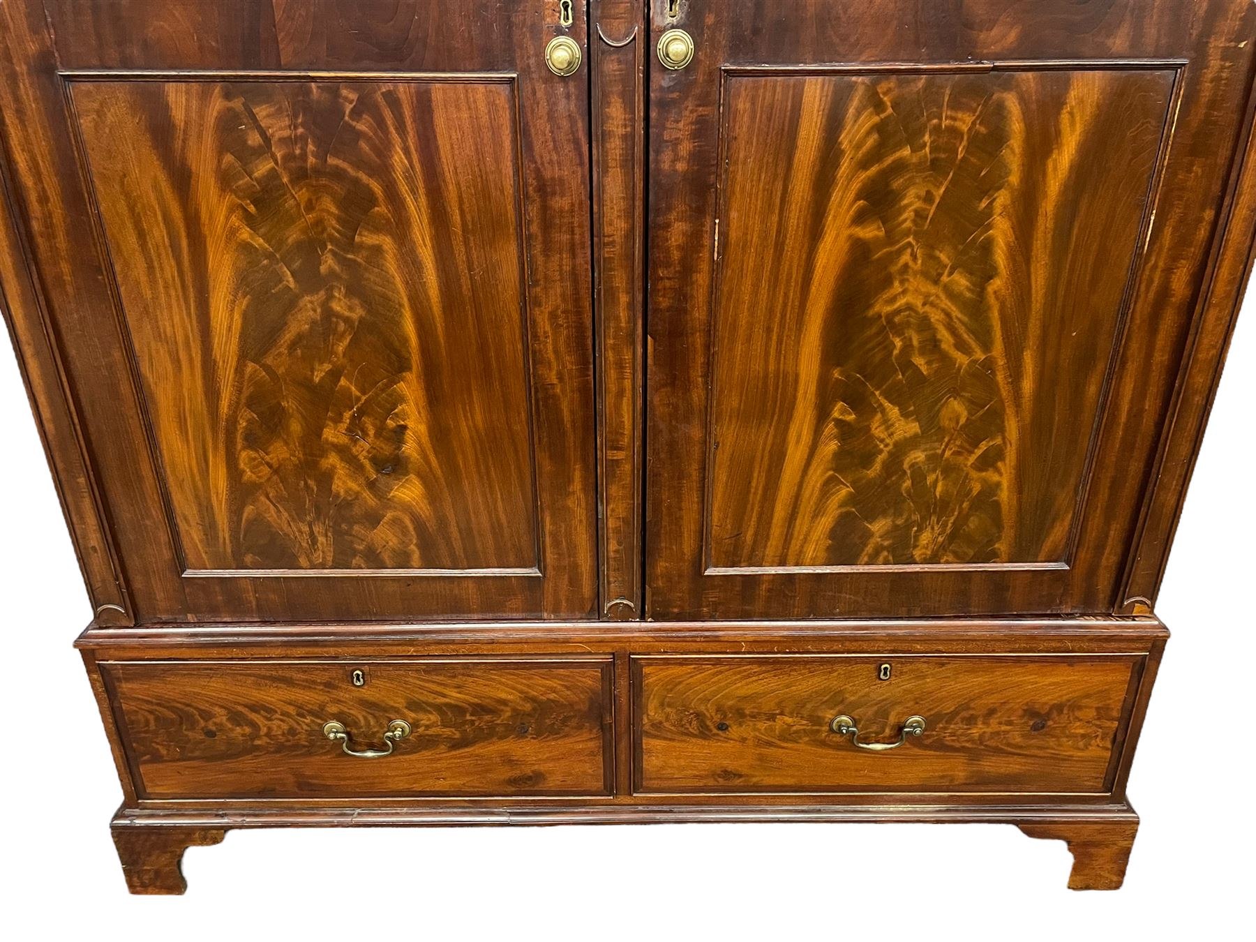 George III mahogany double wardrobe, the projecting cornice with dentil moulding over two panelled doors with mirror-lined interiors, enclosing hanging rails and brass hooks, the base fitted with two drawers, raised on bracket feet