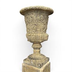 Pair of George III design antiqued composite stone garden urns of campana form, the egg-and-dart everted rim over a waisted body relief moulded with scrolling fruiting foliage and flowerheads, the gadrooned underbelly with twin mask ornaments, the knopped stems on fluted socles, raised on faux panelled square pedestal bases