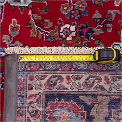 North East Persian Mesued hand-knotted carpet, deep red field with a finely drawn central elongated medallion of navy and ivory, issuing delicate scrolling vines, palmettes and floral sprays in a dense all-over composition, main border on dark ground decorated with a continuous palmette and vine scroll, flanked by multiple narrow guard stripes incorporating rosettes and stylized floral devices, with cotton fringe ends 