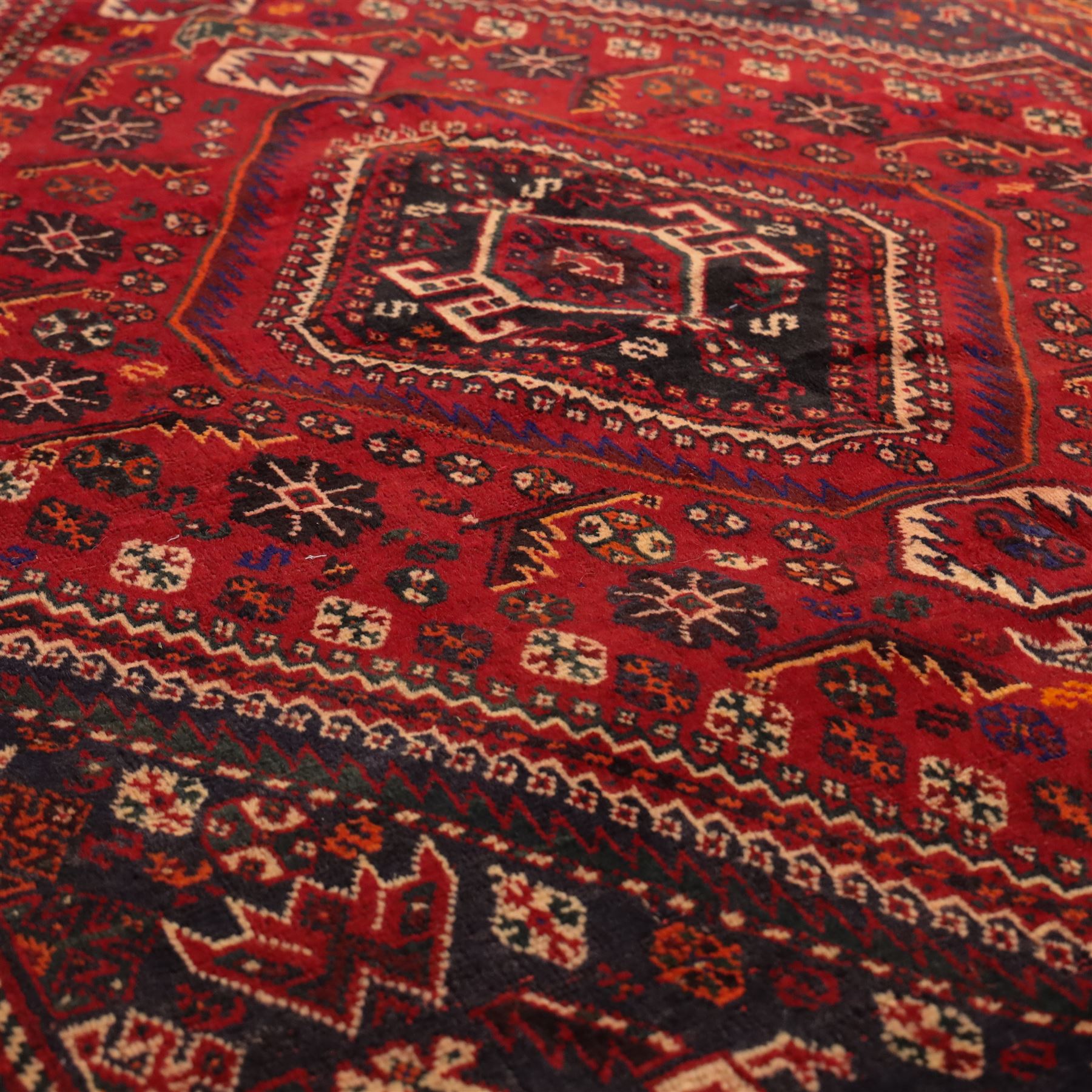 South West Persian Qashqai hand-knotted rug, madder red field with a large stepped diamond medallion with scattered geometric devices and indigo spandrels filled with geometric motifs, framed by multiple narrow guard borders and broad main border, wool fringe ends 