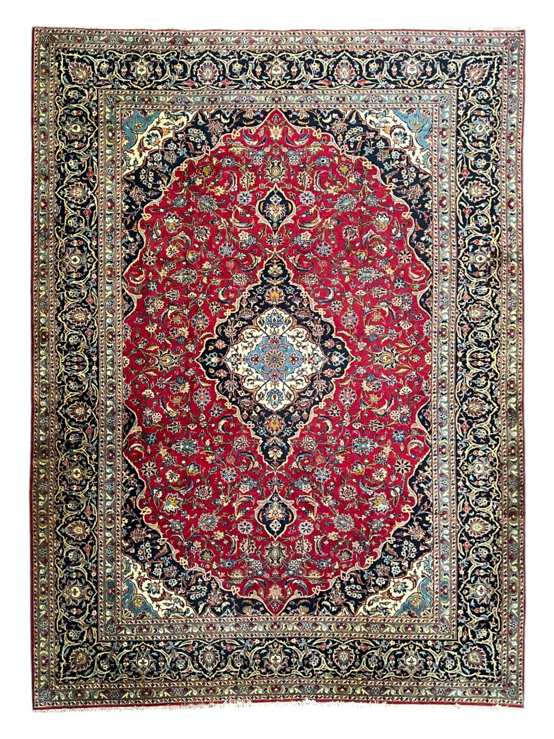 Persian Kashan crimson ground carpet, the central pole medallion decorated with flower heads, surrounded by trailing leafy branches and palmettes, scrolling border decorated with further palmettes, within floral pattern guard stripes 