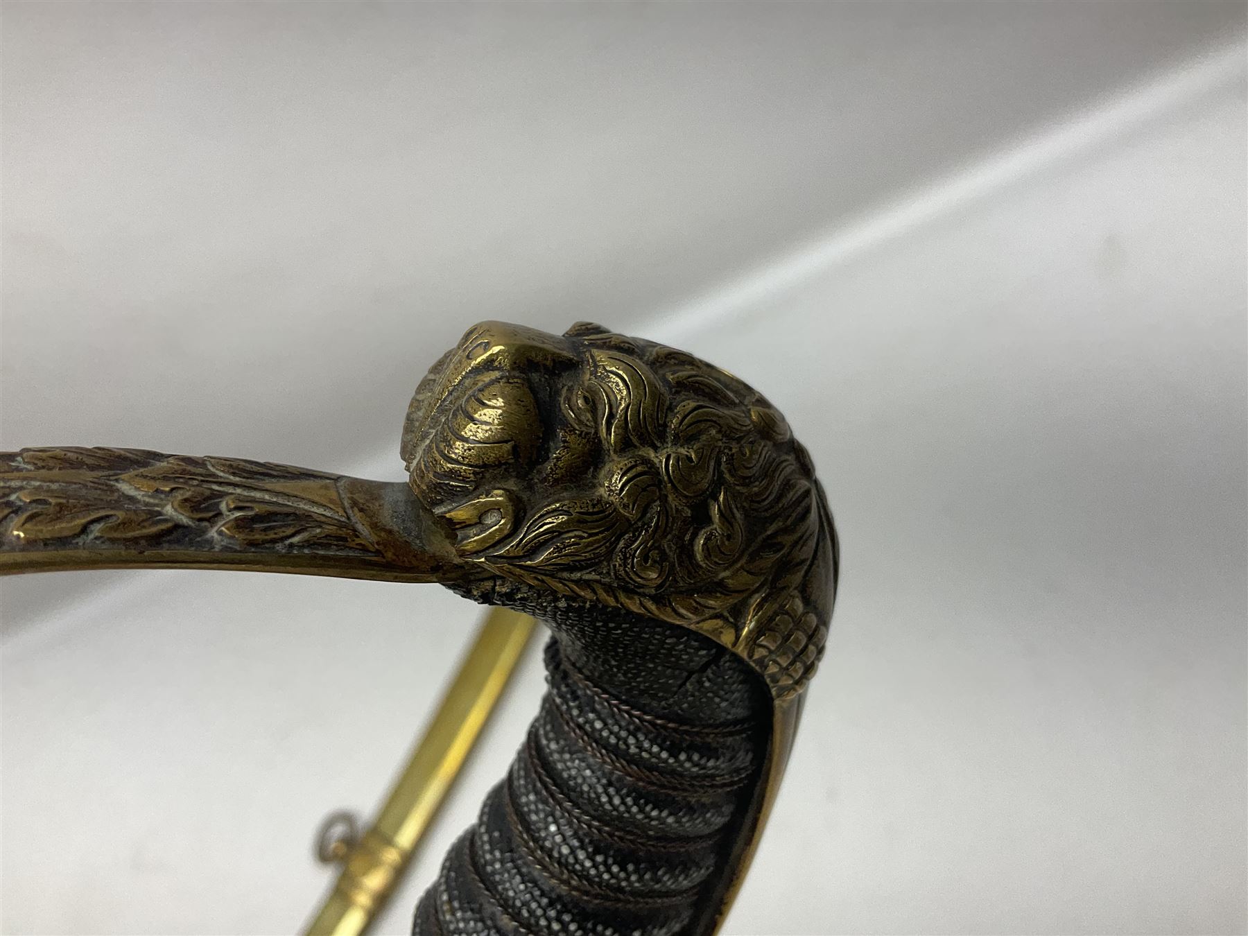 German Saxon 1st Empire Light Cavalry officer's sword c1820s, the 79cm clipped curving blade engraved with the crest of Hanover and various battle trophies with traces of blueing and gilding, brass hilt with knucklebow, foliate square langets, ornate downswept quillon, wire-bound fish skin grip with lion's head pommel; in brass scabbard with two suspension rings L95cm overall