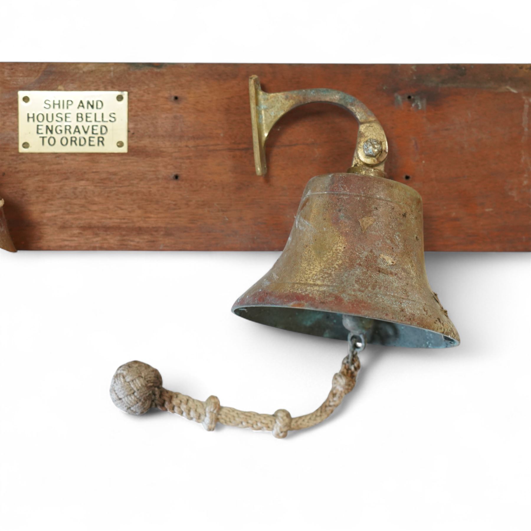 Set of three brass ship bells, each with wall bracket and two with rope pulls, mounted on a rectangular mahogany backboard with brass plaque inscribed ‘Ship and House Bells Engraved to Order’