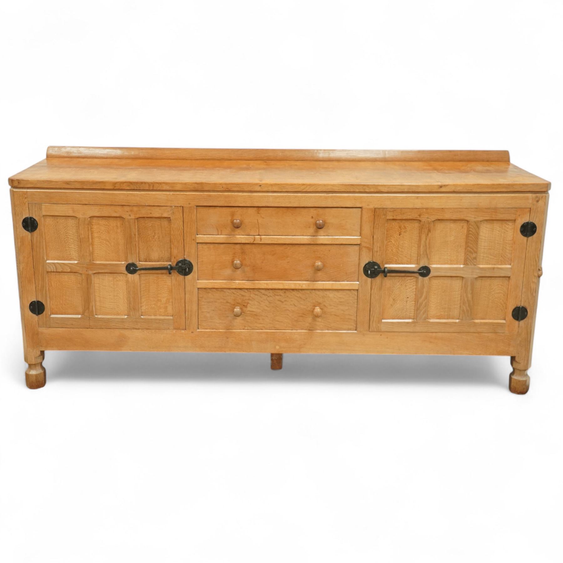 Mouseman - oak sideboard rectangular adzed top with raised back over three central drawers and two flanking cupboards, enclosed by panelled doors with wrought metal fixtures, the canted upright carved with mouse signature, on octagonal feet, by the workshop of Robert Thompson, Kilburn