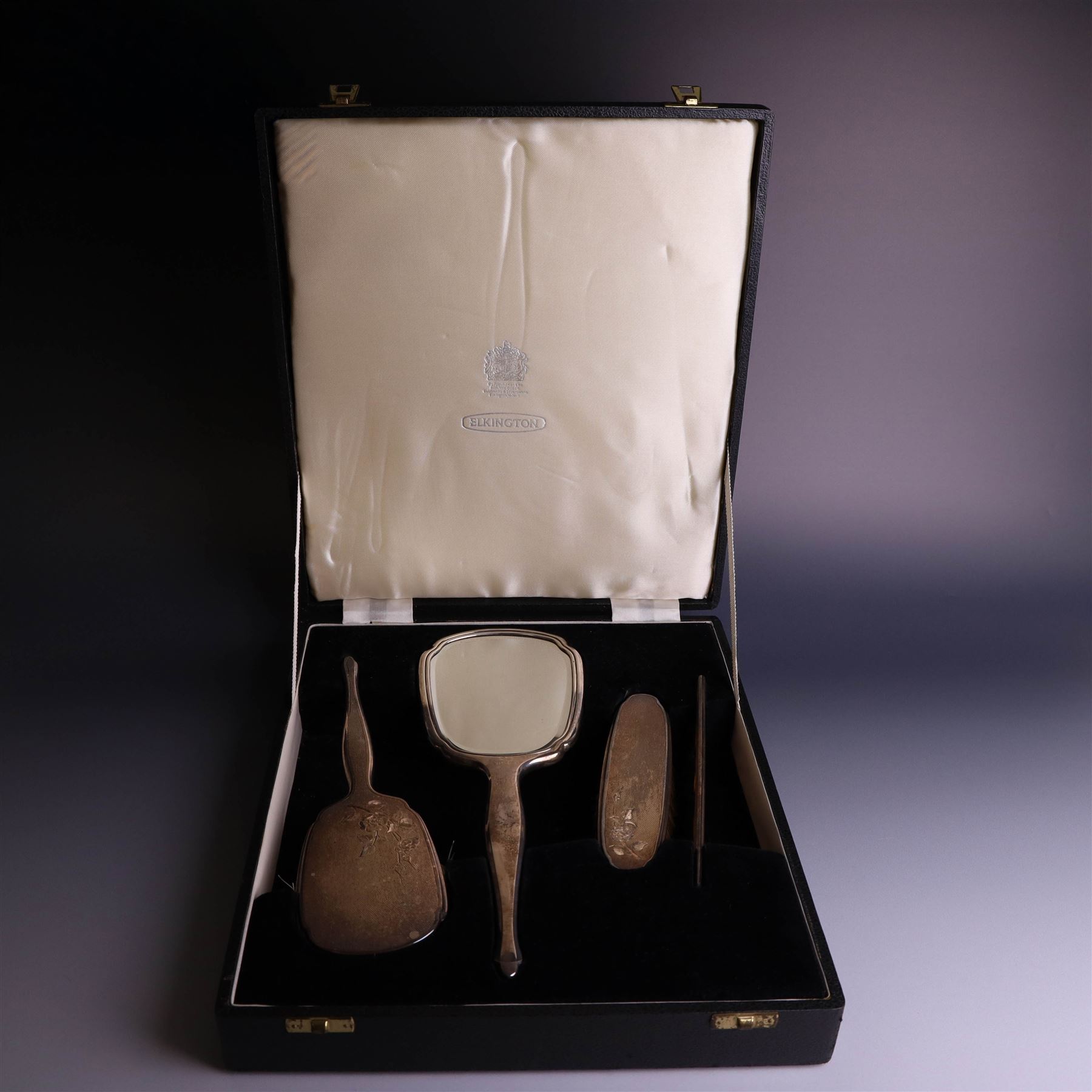 20th Century silver mounted dressing table set, comprising hand mirror, clothes brush, hairbrush and comb holder, each with engine turned and engraved floral decoration, three pieces hallmarked Adie Brothers Ltd Birmingham 1964, the comb holder hallmarked Elkington & Co Ltd Birmingham 1965, contained within a fitted tooled leather case
