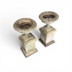 Pair of weathered cast stone Neoclassical design garden Kylix shape urns, foliate moulded rim over a gadrooned underbelly, the scalloped socle over a rectangular pedestal with faux-panelled sides, stamped with stylised ‘H’ monogram