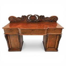 Mid Victorian mahogany pedestal sideboard, the rectangular top with raised back centred by a carved shell within scrolling acanthus and foliate cresting, over a central shaped frieze drawer flanked by two short drawers, above a kneehole recess, flanked by panelled cupboard doors with carved corbel supports, enclosing shelved interiors