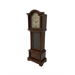 A miniature spring driven longcase clock made in Germany by the Hamburg American Clock Company c 1890, with a mahogany finished case, break arch pediment and opening hood door, case with a fully glazed opening trunk door on a short plinth with raised feet, with an etched silver effect dial, Arabic numerals, minute track and spade hands, 8-day key wound movement with a silk suspension and visible pendulum.




