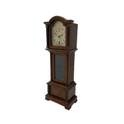 A miniature spring driven longcase clock made in Germany by the Hamburg American Clock Company c 1890, with a mahogany finished case, break arch pediment and opening hood door, case with a fully glazed opening trunk door on a short plinth with raised feet, with an etched silver effect dial, Arabic numerals, minute track and spade hands, 8-day key wound movement with a silk suspension and visible pendulum.




