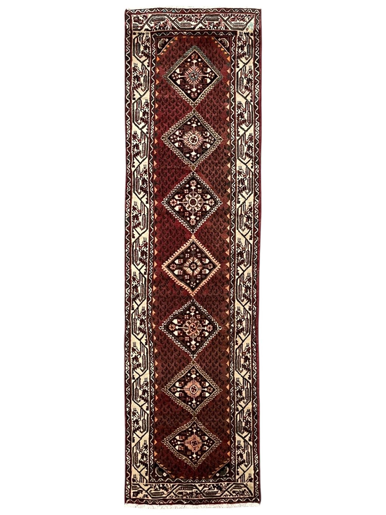 Persian Baluch red ground runner, seven lozenge medallions each decorated with stylised floral motifs, ivory border decorated with trailing pattern and Boteh motifs, within geometric guard stripes 