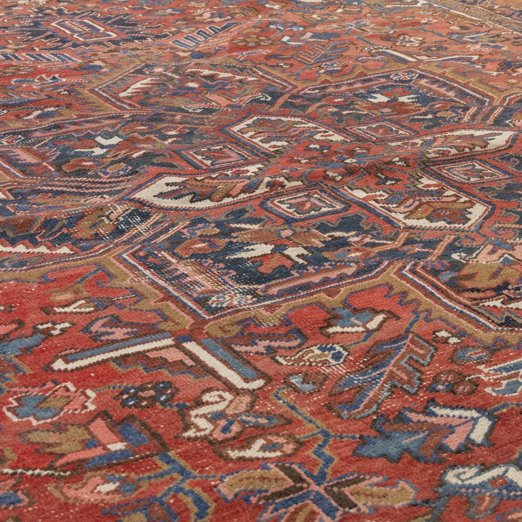 Persian Heriz carpet, red ground with large central geometric medallion, angular flowering branches and stylised foliate decoration, within a broad dark blue floral border and narrow guard stripes