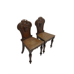 Pair Victorian oak hall chairs, scallop shaped back with carved scrolls and central shield moulding, panel seat over shaped frieze rail, raised on turned supports