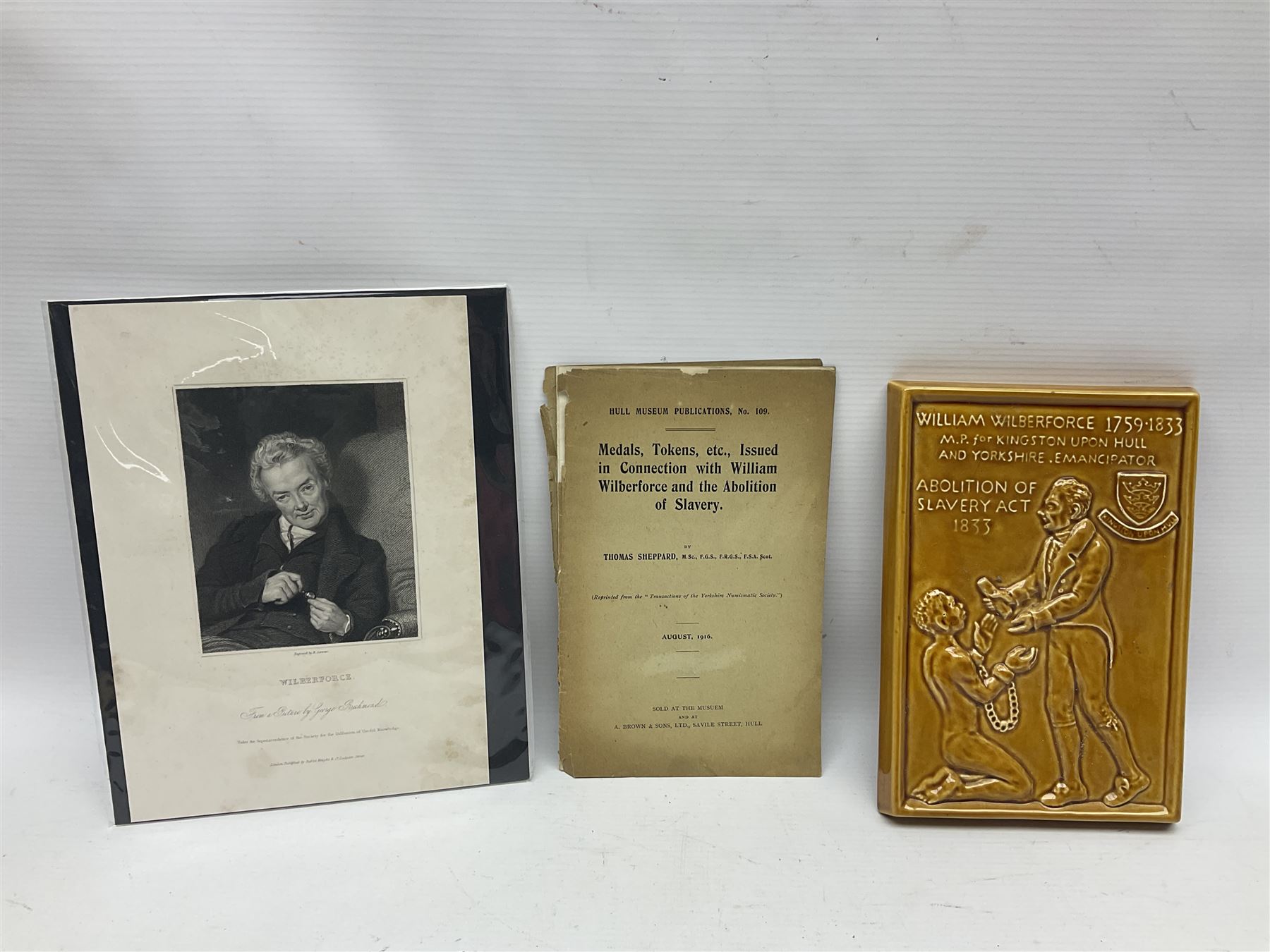 Group of William Wilberforce Abolition of Slavery items, comprising Wedgwood black on cane Jasperware pin tray, Wedgwood light blue Jasperware plate, and two Wedgwood oval medallion pendants, each depicting a kneeling figure beneath the inscription 'AM I NOT A MAN AND A BROTHER?', an Eastgate pottery plaque decorated in relief with a kneeling figure before William Wilberforce, a Hull Museum Publications pamphlet titled 'Medals, Tokens, etc., Issued in Connection with William Wilberforce and the Abolition of Slavery', by Thomas Sheppard, dated 1916, and an antique print depicting William Wilberforce after the original portrait by George Richmond, (7)
